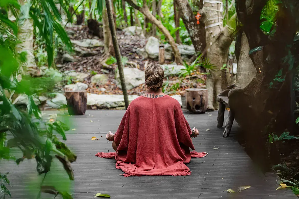 Person meditating on a wooden platform surrounded by forest.